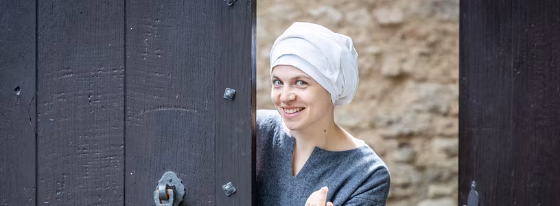 Eine mittelalterlich gekleidete Magd steht im Tor von Schloss Habsburg und winkt hinein..