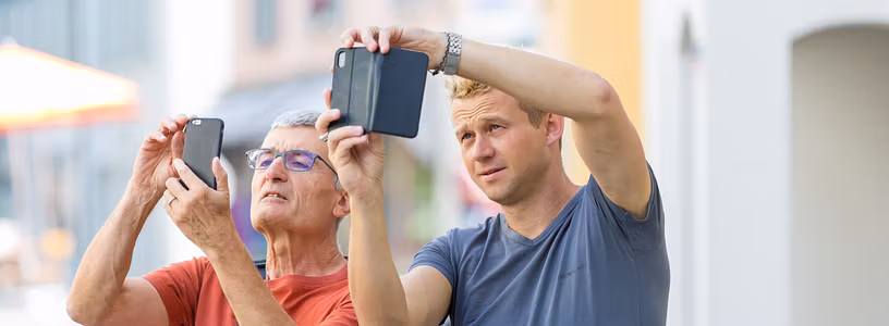 Zwei Männer halten ihre Handys in die Höhe und blicken auf das Display.