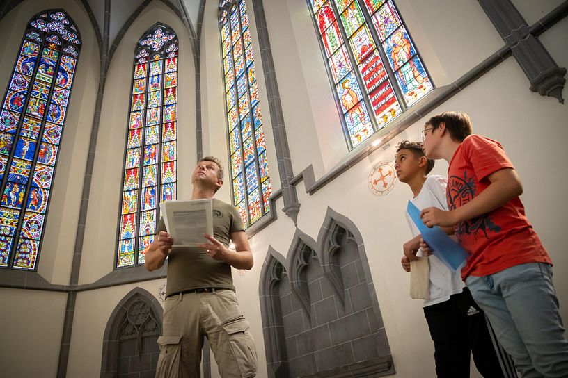 Ein Mann und zwei Jungen stehen im Kloster Königsfelden vor den Glasfenstern