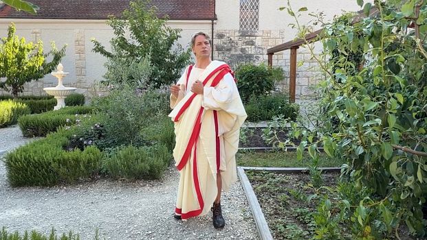 Der Kommandant Vindonissa steht im Garten. Er trägt eine Toga.
