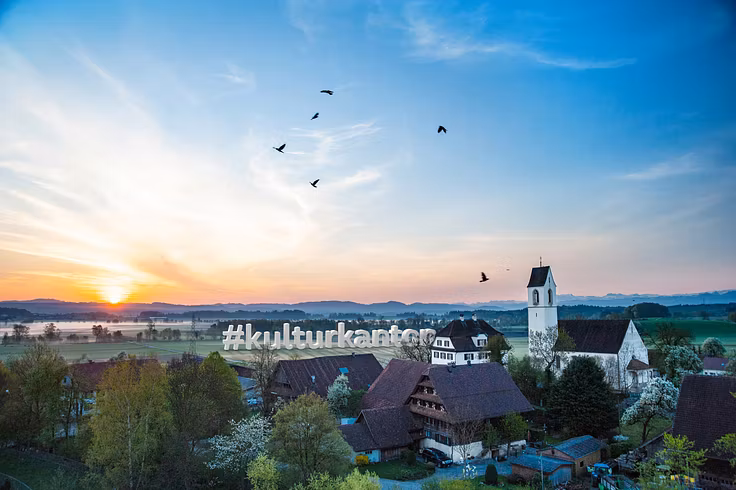 Idyllische Landschaftsaufnahme mit der Sonne am Horizont, im Vordergrund die alte Kirche Boswil