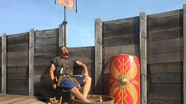 Ein Legionär sitzt auf einem Stuhl und blickt entspannt in die Sonne. Seine Füsse baden in einem Bottich mit Wasser.