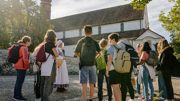Eine Klostermagd steht mit einer Gruppe Schülerinnen und Schülern vor dem Kloster Wettingen.