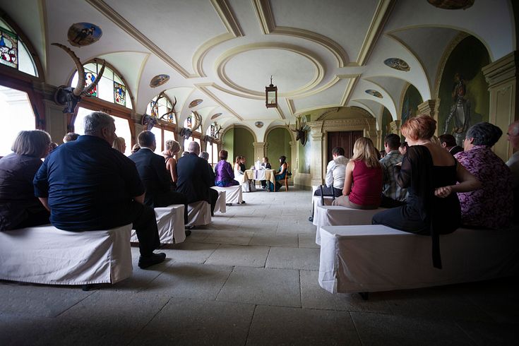 Traulokal "Eingangshalle" Schloss Wildegg: Viele Gäste einer zivilen Trauung von hinten, vorne ein Tisch mit Brautpaar und Standesbeamtin. Das Ambiente ist ein alter historischer Raum, links eine grosse Fensterfront.