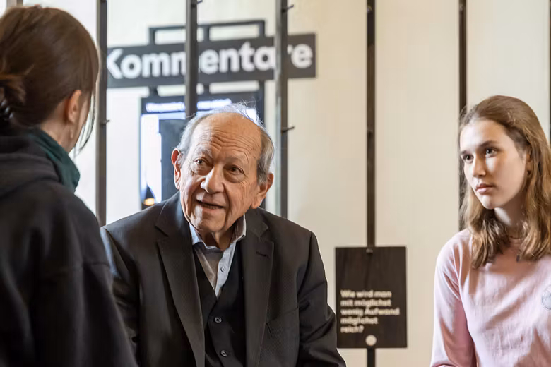 Ausstellungsraum im Parlatorium der Klosterhalbinsel Wettingen: Ein älterer Mann im Gespräch mit zwei Schülerinnen.