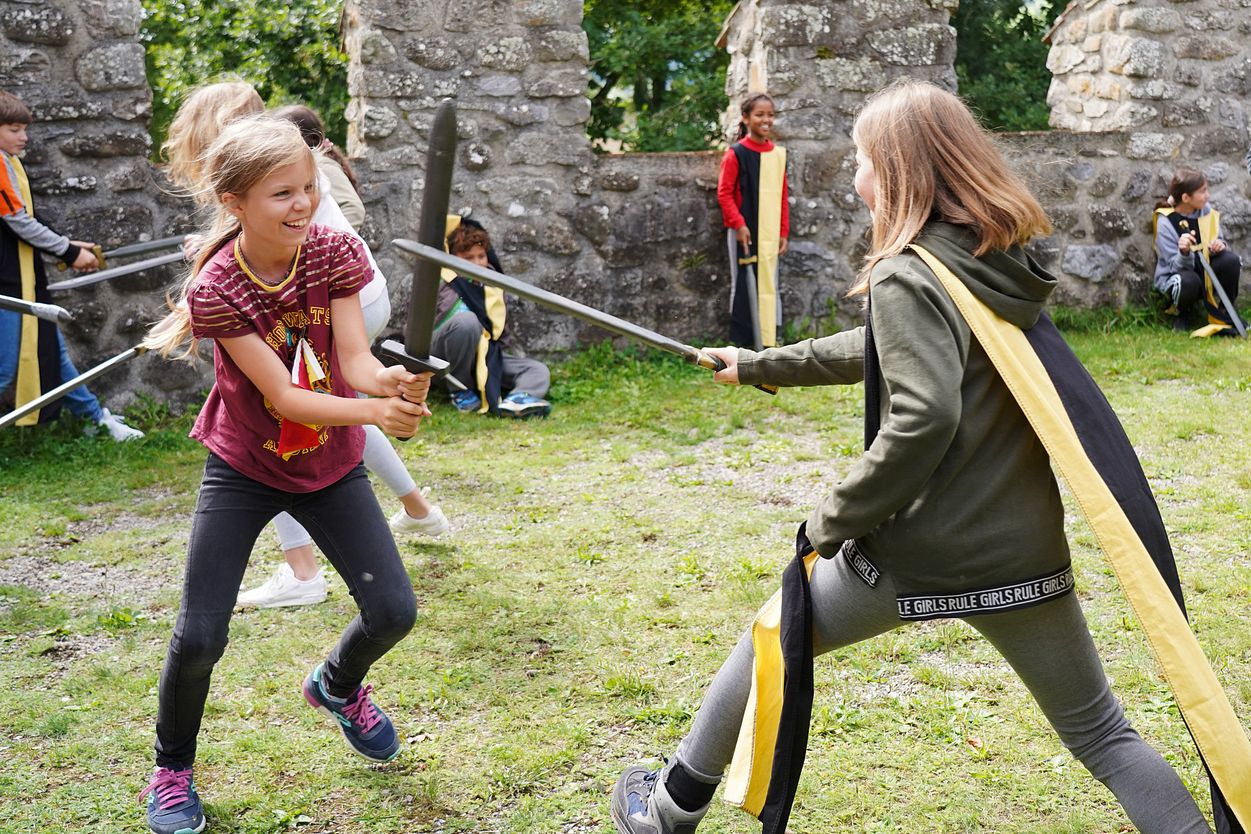 Workshop "Feste Burg Schloss Hallwyl" Kinder haben zusammen spass im Schwertkampf mit Zinnen im Hintergrund