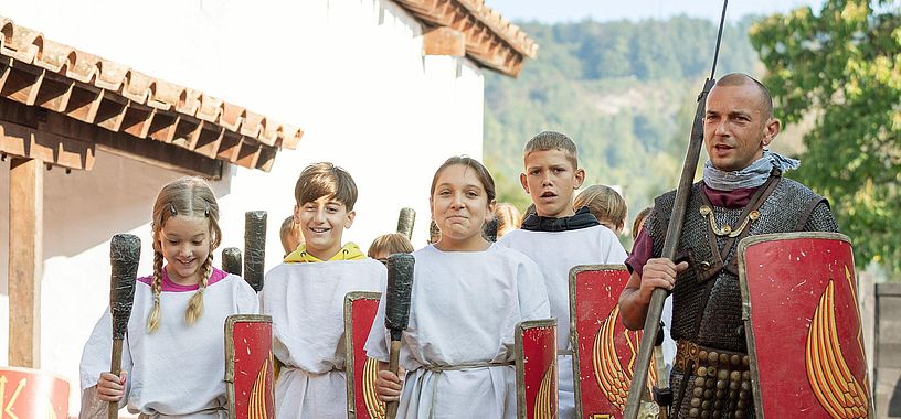 Ein Legionär marschiert mit einer Gruppe Mädchen und Buben nebeneinander wie die Römer.
