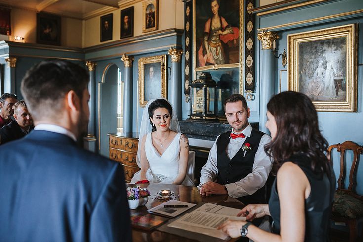Zivile Trauung im Salon von Schloss Wildegg: Ein Brautpaar sitzt mit einer Standesbeamtin sowie weiteren Personen an einem Tisch. Dahinter ist ein Teil des historischen Raumes im Museum zu sehen.
