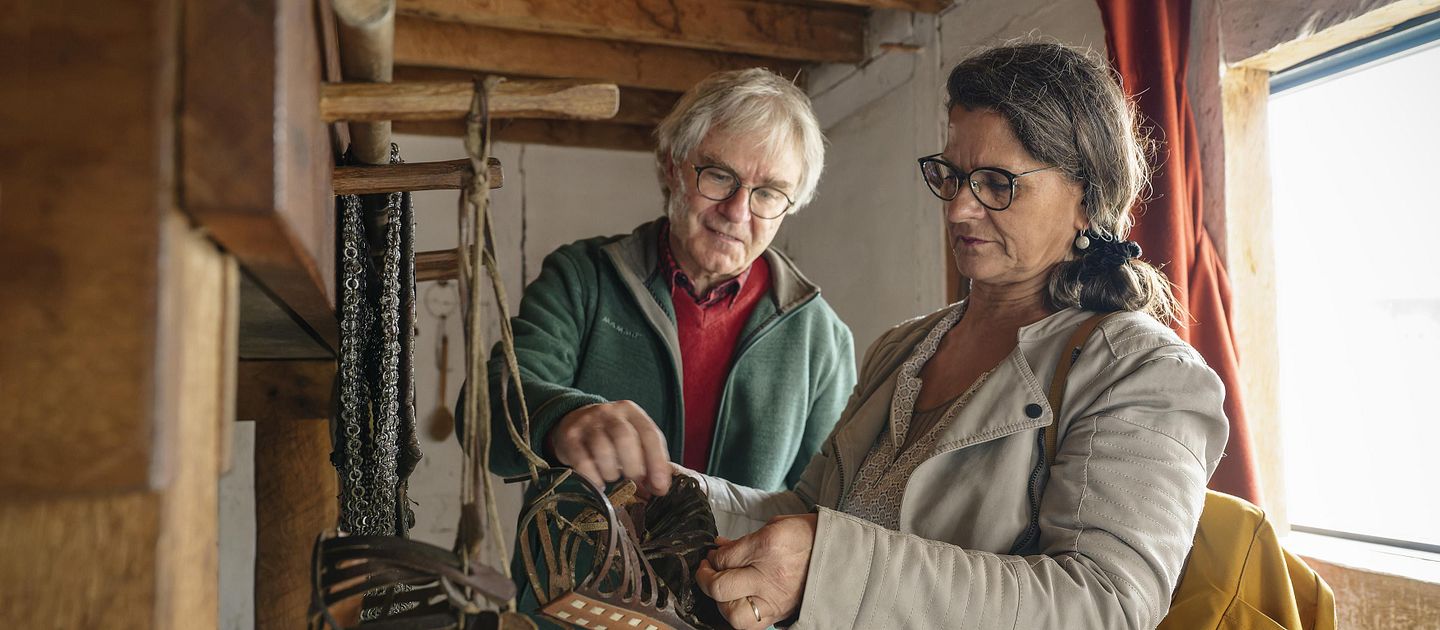 Ein Mann und eine Frau stehen in einer römischen Legionärsunterkunft. Sie betrachten römische Sandalen.