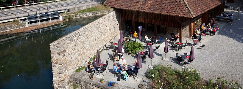 Blick von oben auf den Aussenbereich des Cafés von Schloss Hallwyl. An den Tischen im Schlosshof sitzen Besucherinnen und Besucher. Das Wetter ist sommerlich.