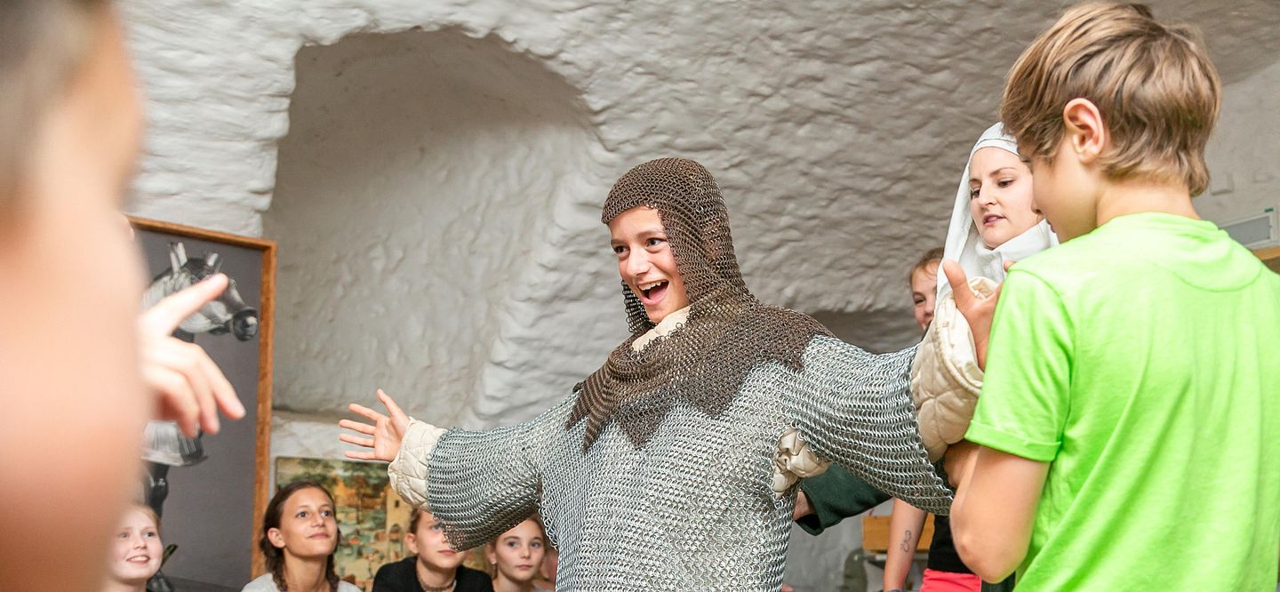 Gruppe von Kindern umringen einen Jungen, der ein Kettenhemd angezogen hat auf Schloss Lenzburg