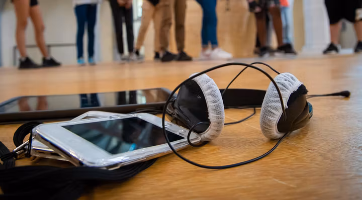 Audioguide-Gerät mit Kopfhörer, im Hintergrund in Unschärfe Schülerinnen und Schüler.