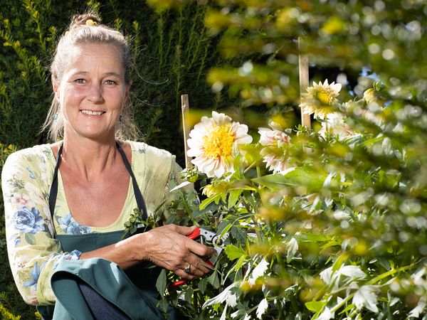 Porträt von Tanya van der Laan. Sie kniet neben einer Pflanze im Garten von Schloss Wildegg und hält eine kleine Gartenschere.