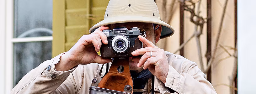 Ein Mann im Expeditionsoutfit mit Kamera vor dem Gesicht. Er fotografiert.