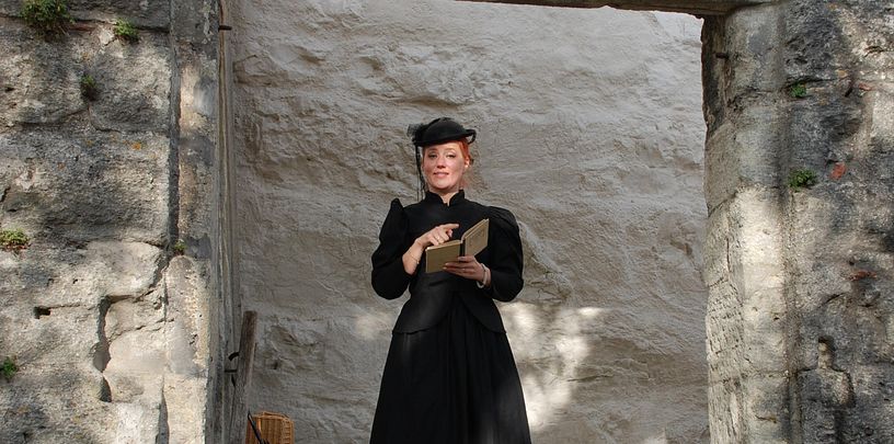 Eine als Gouvernante verkleidete Frau mit Buch auf Schloss Wildegg (blickt direkt in die Kamera)