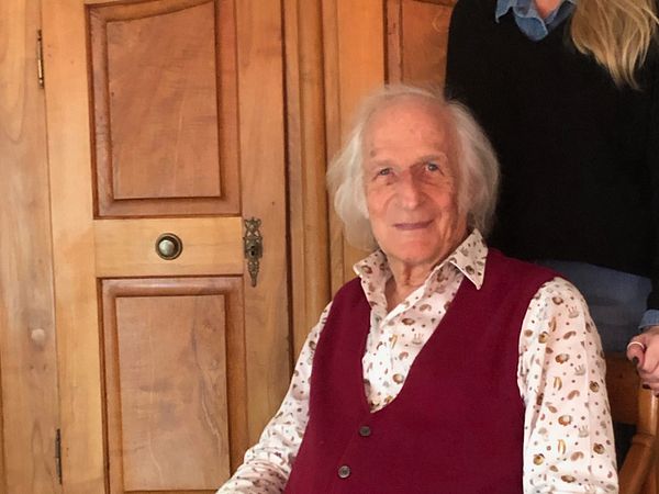 Gerôld Müller sitzt auf einem Stuhl, im Podcast von Museum Aargau. Eine Frau mittleren Alters steht hinter ihm und hat die Hände auf die Stuhllehne gelegt.