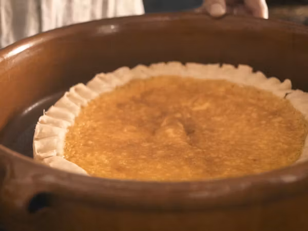 Zwei Hände halten einen Topf mit Safran-Sahne-Torte in der Mittelalterküche von Schloss Lenzburg.