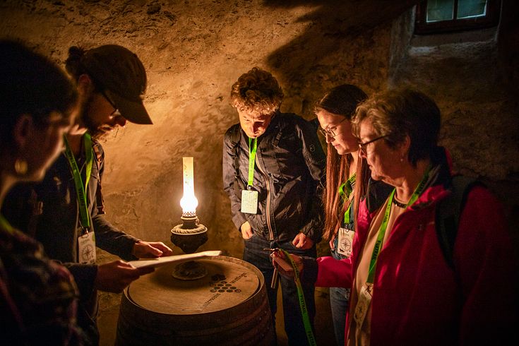 Mehrere Personen auf dem Foxtrail Klosterhalbinsel Wettingen. Die Gruppe steht in schummrigem Licht um ein Fass, der Raum ist von einer Lampe erleuchtet.