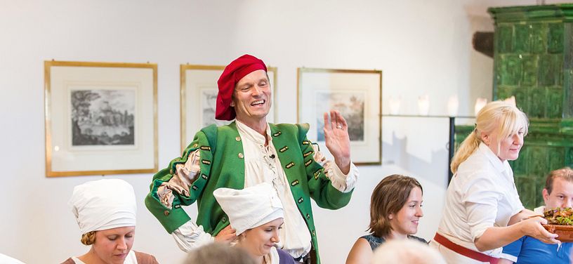 Ein Schauspieler stehen in historischer Kleidung, um ihn herum Gäste in einem Restaurant