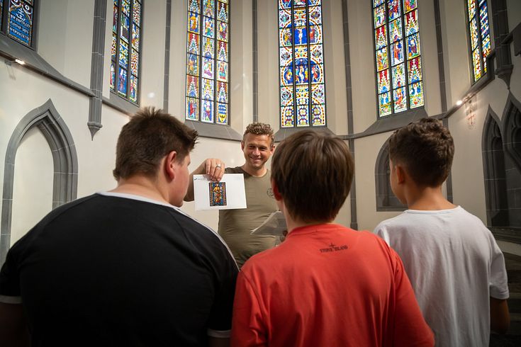Ein Museumsführer spricht zu Schülern in der Klosterkirche Königsfelden, im Hintergrund die berühmten Glasfenster.