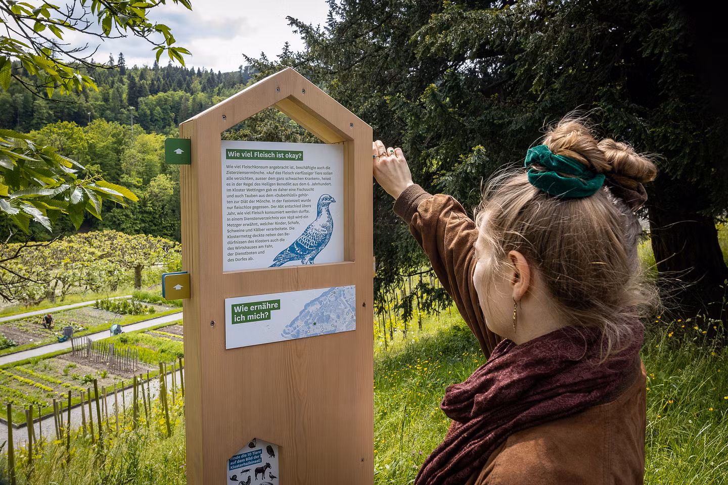 Eine Frau steht vor einer Info-Stele mit Textinformationen inmitten dem Garten der Klosterhalbinsel Wettingen.