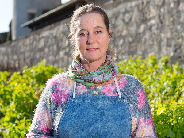 Eine Frau steht mit Gärtnerinnen-Kleidung im Garten.