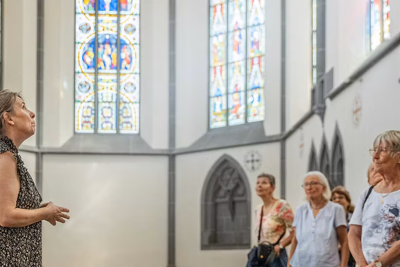 Eine Museumsführerin mit einer Gästegruppe im Chor der Klosterkirche Königsfelden; im Hintergrund die berühmten Glasfenster.