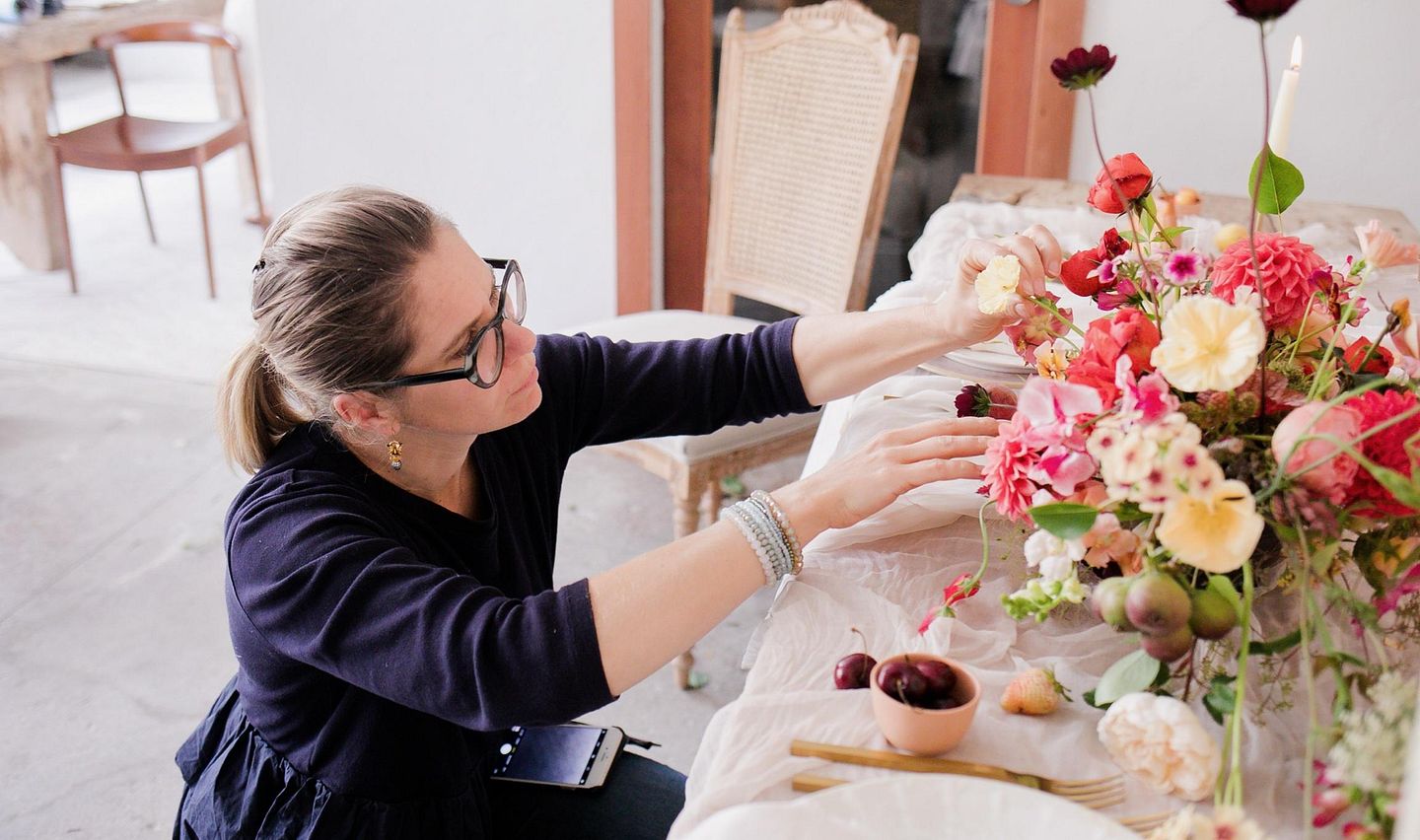 Floristin Evelyn Krebs kniet vor einem Tisch mit einem Blumenstrauss und richtet einzelne Blumen aus.