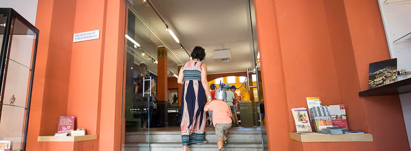 Besucher*innen betreten das Vindonissa Museum mit der grossen Orangen Eingangstüre