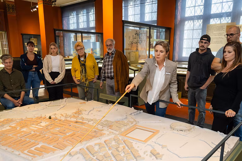Eine Gästegruppe mit Museumsführerin. Die Gruppe steht um ein grosses Modell des Legionslagers Vindonissa.