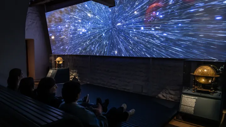 Ausstellung "Observatorium" auf der Klosterhalbinsel Wettingen: Grosse Leinwand mit Sternenhimmel, davor Schülerinnen und Schüler im dunklen Zuschauerraum.
