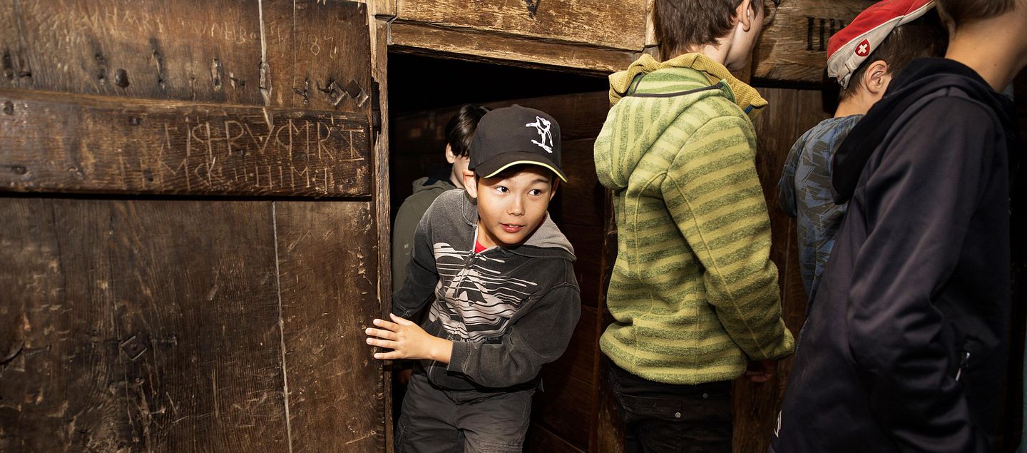 Ein Bub tritt aus einem Raum im Gefängnis von Schloss Lenzburg. Vor ihm sind weitere Schülerinnen und Schüler zu sehen.