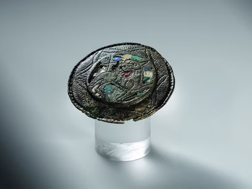 Scheibenfibel aus Buntmetall mit farbigen Emaille-Einlagen. Eingraviert ist das Lamm Gottes – ein Sinnbild für die Auferstehung Christi.