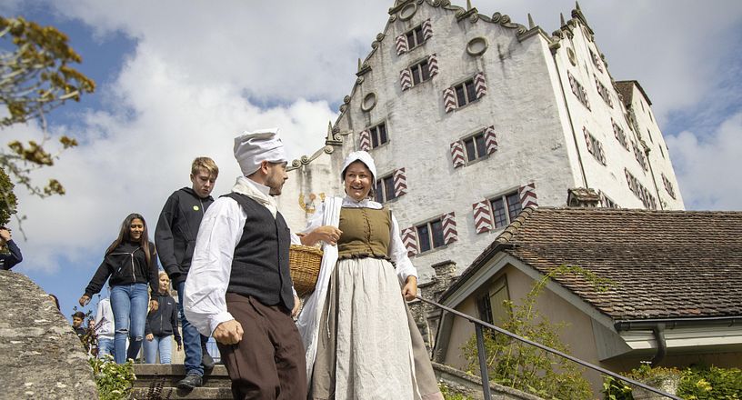 Eine Magd und ein Knecht auf einer Treppe, im Hintergrund Schloss Wildegg