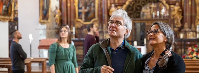 Ein Ehepaar steht in der Klosterkirche Wettingen und blickt staunend in die Höhe. Dahinter weitere Personen in Unschärfe.