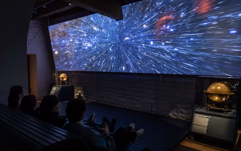 Ausstellung "Observatorium" auf der Klosterhalbinsel Wettingen: Grosse Leinwand mit Sternenhimmel, davor Schülerinnen und Schüler im dunklen Zuschauerraum.