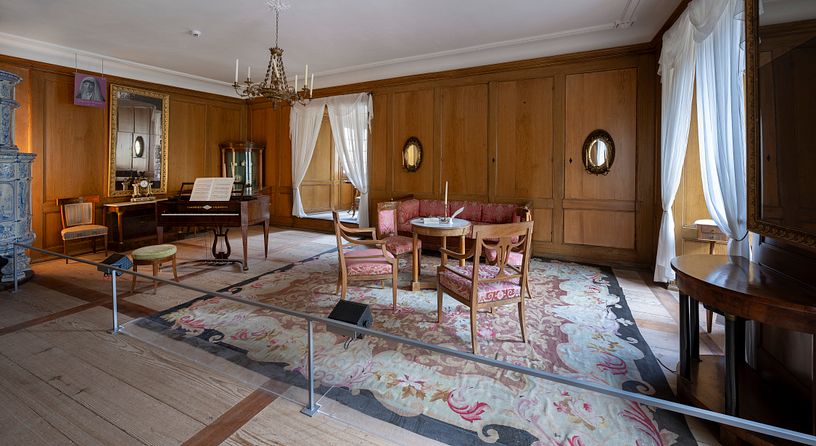 Ein Raum im Wohmuseum von Schloss Hallwyl mit Teppich, Klavier und weiteren Möbeln.