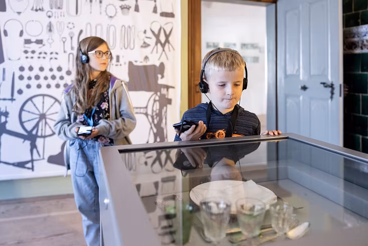 Zwei Kinder mit Kopfhörer in der Ausstellung von Schloss Hallwyl.
