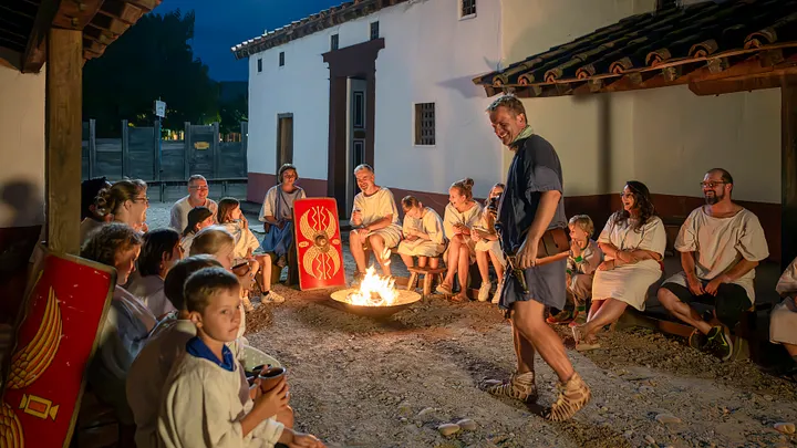 Römisch gekleidete Männer und Frauen nachts an einem Lagerfeuer in historischer Kulisse