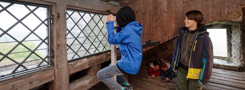 Zwei Schüler unter dem Dach von Schloss Habsburg; ein Bub blickt durch ein Fernrohr ins Weite.