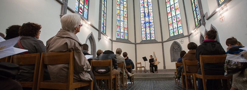 Blick in den Chor der Klosterkirche Königsfelden mit ihren Glasfenstern. Vorne auf der Bühne spielt eine Musikerin, der Chor ist gefüllt mit Zuhörerinnen und Zuhörern.