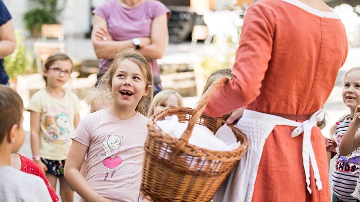 Eine Gruppe Kinder steht vor einer Magd, ein Mädchen lächelt freudig.