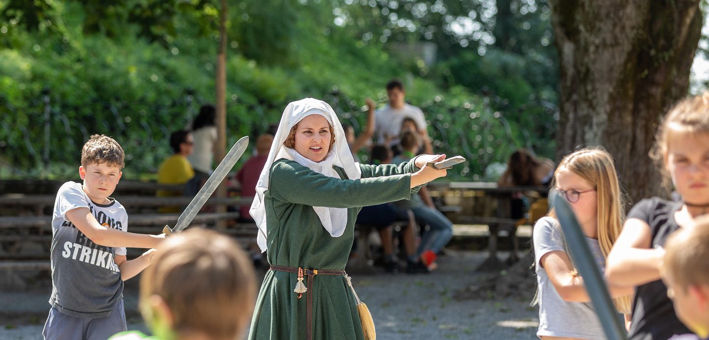 Kinder üben den Umgang mit dem Schwert bei der Ritterausbildung mit einer mittelalterlich gekleideten Frau
