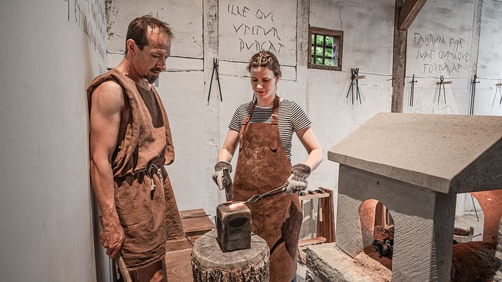Ein römischer Schmied und eine Helferin schmieden im Legionärspfad Vindonissa (Schmiede) Eisen.