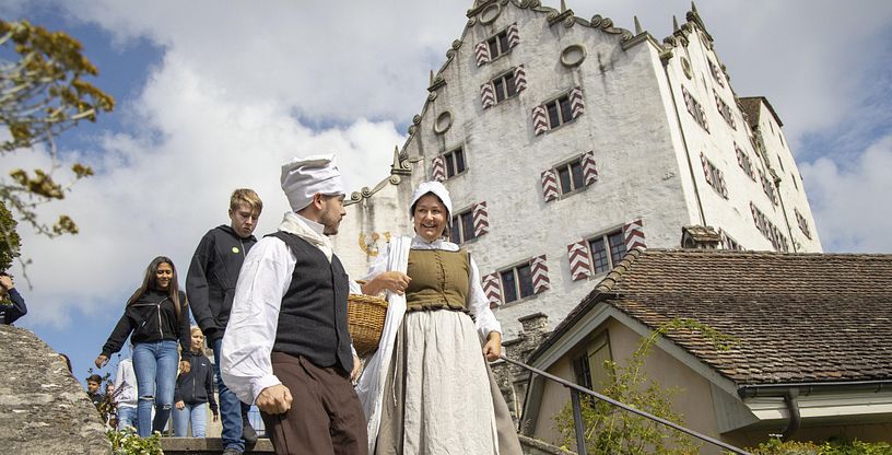 Eine Magd und ein Knecht auf einer Treppe, im Hintergrund Schloss Wildegg