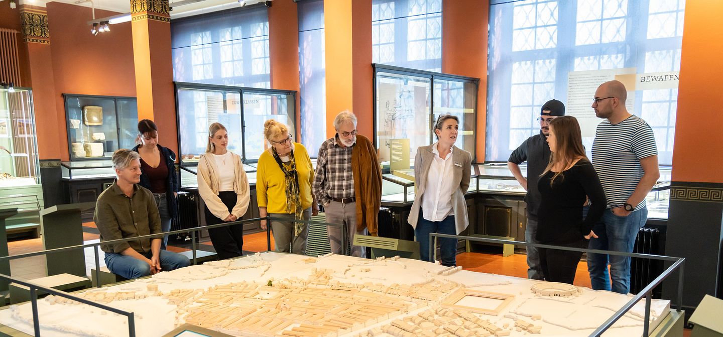 Führung im Vindonissa Museum. Eine Besuchergruppe steht mit einer Geschichtsvermittlerin um das Lagermodell des Legionslagers Vindonissa