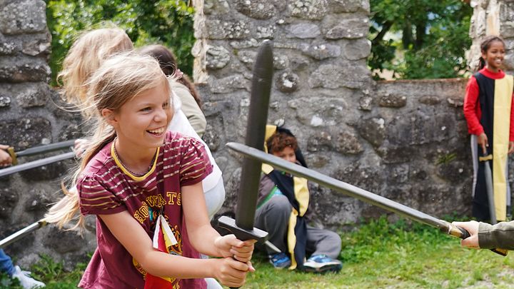 Workshop "Feste Burg Schloss Hallwyl" Kinder haben zusammen spass im Schwertkampf mit Zinnen im Hintergrund