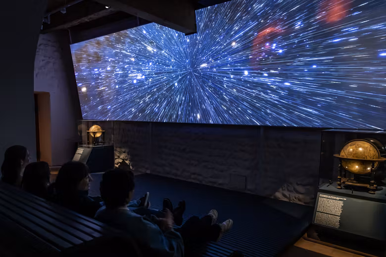 Ausstellung "Observatorium" auf der Klosterhalbinsel Wettingen: Grosse Leinwand mit Sternenhimmel, davor Schülerinnen und Schüler im dunklen Zuschauerraum.