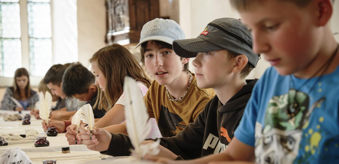 Schülerinnen und Schüler schreiben bei einem Workshop auf der Klosterhalbinsel Wettingen mit traditionellen Gänsekielen (Federkiel).