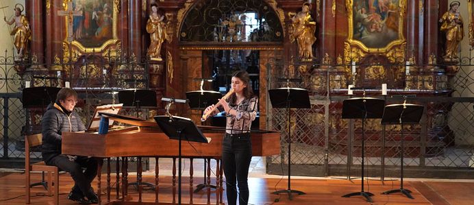 Eine Person spielt Klavier und eine andere Person spielt Flöte in einer Kirche. 